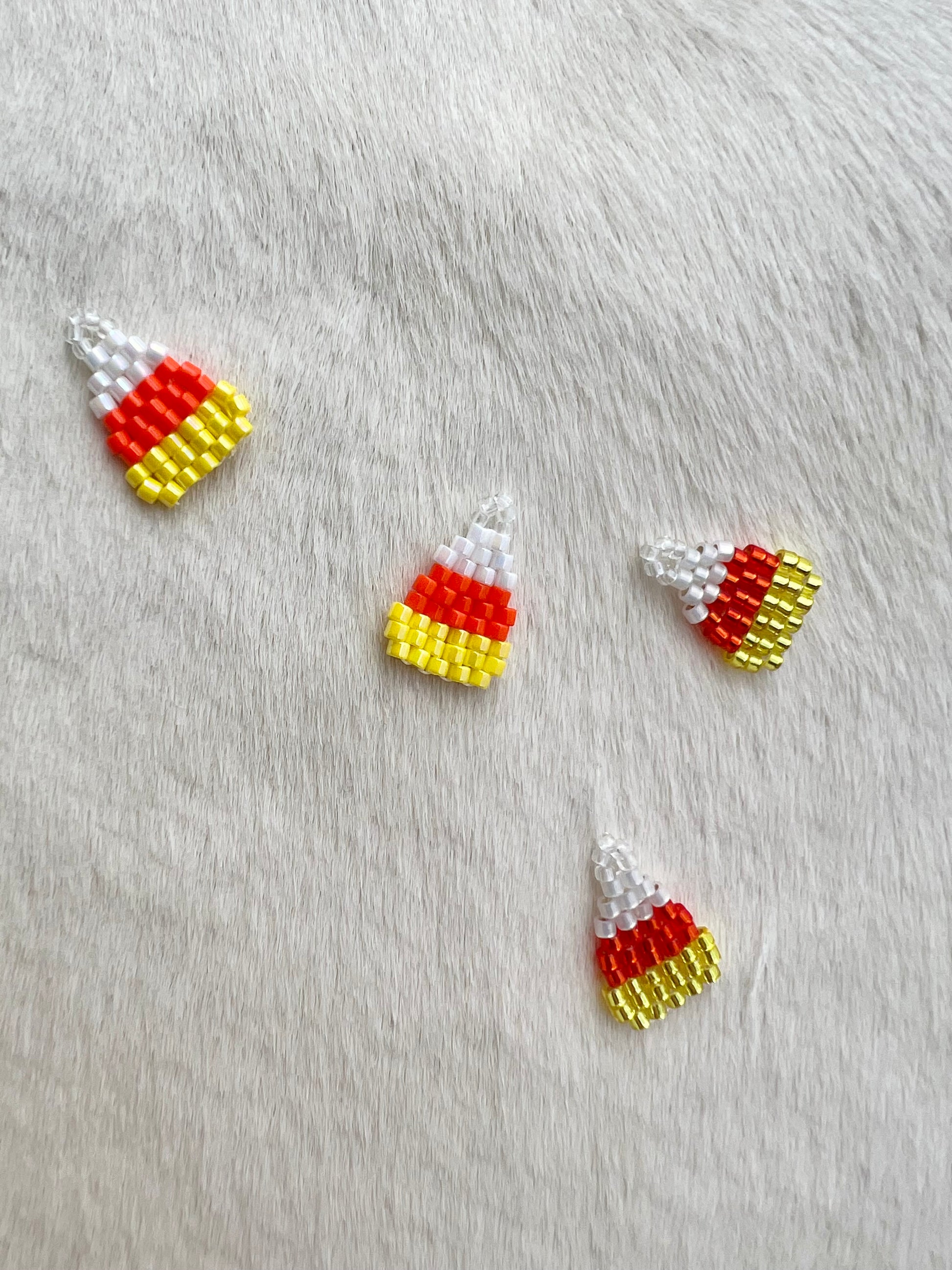 Candy corn-shaped beaded charms on a gray fabric background