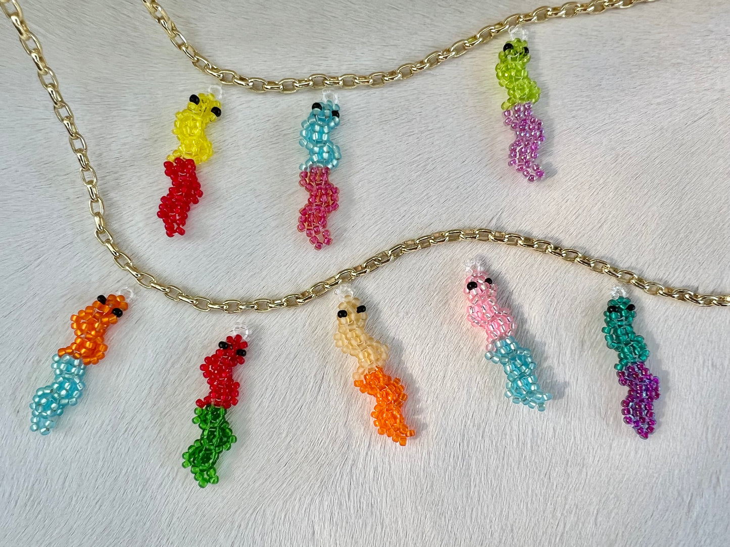 Colorful beaded gummy worm charm necklaces on a gold chain against a white background