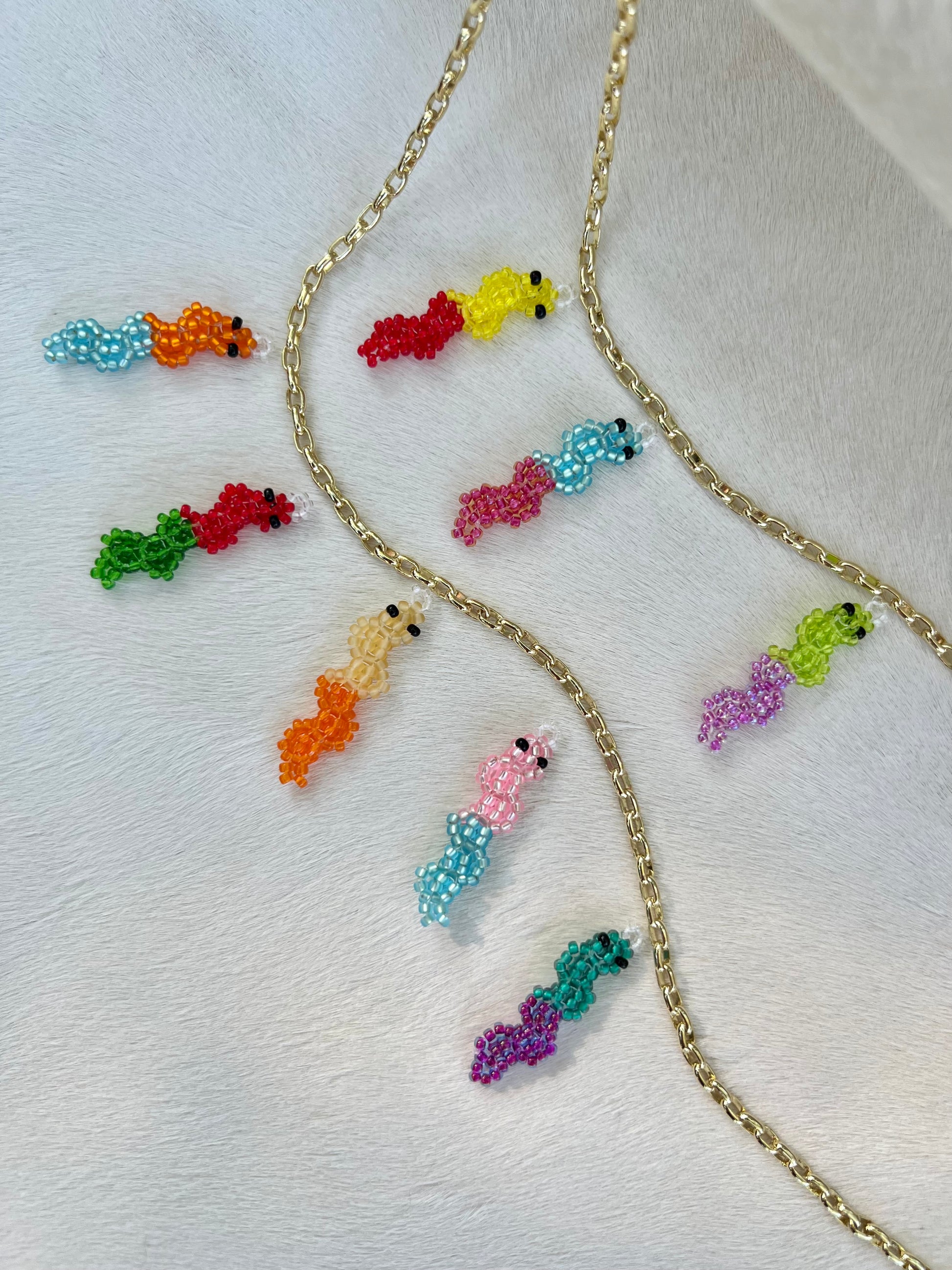 Colorful beaded gummy worm pendants on a gold chain against a white background