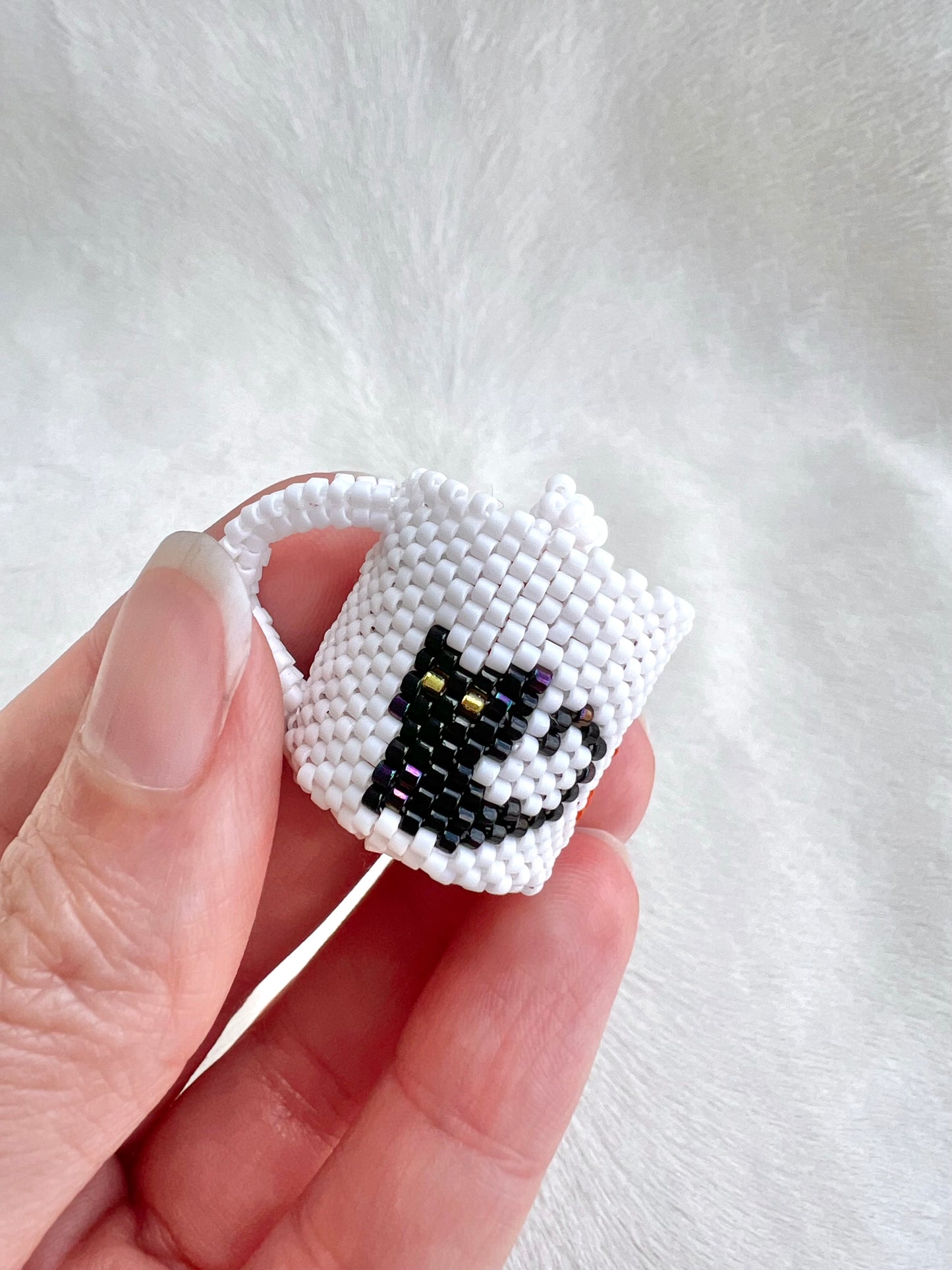 Hand holding a small white and black beaded mug against a white background