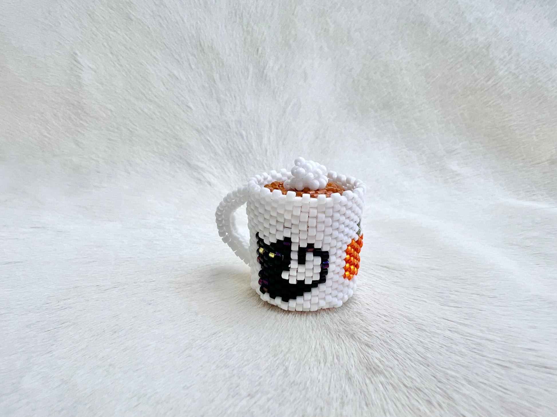 Small white beaded cup with a black cat face design on a white fur background