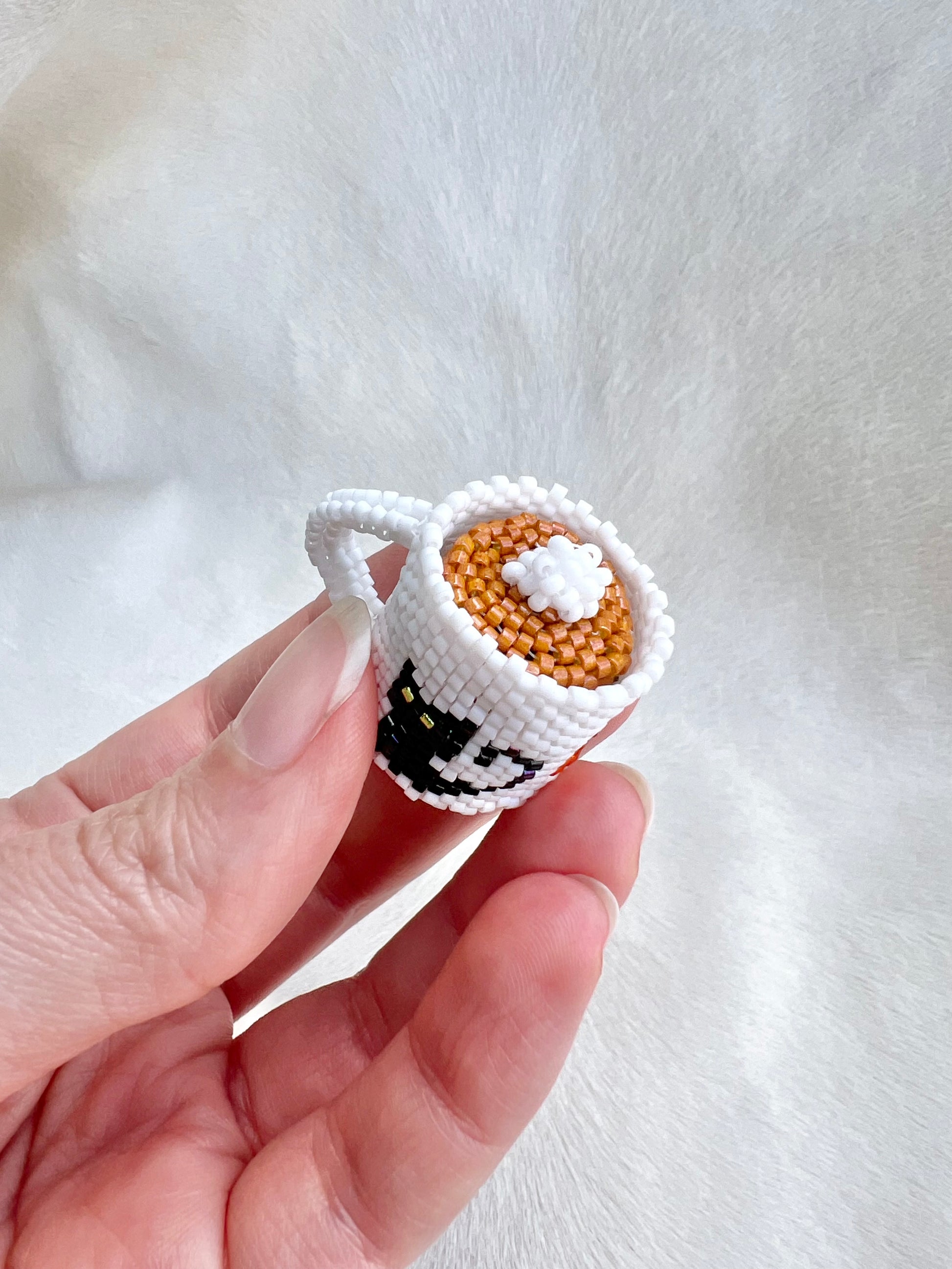 Hand holding a small hand beaded cup with a cat design on a white background
