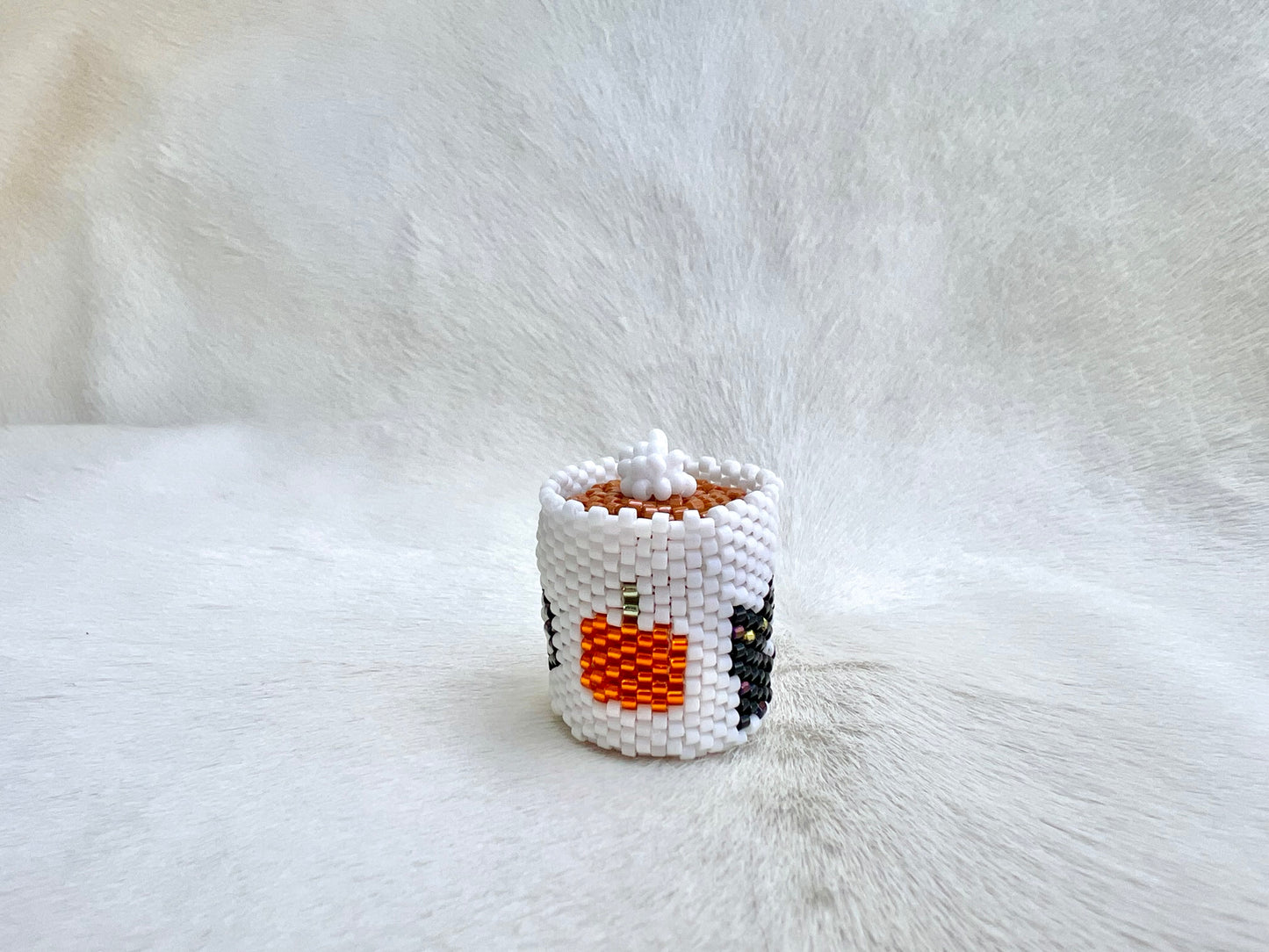 Small white beaded mug with a pumpkin design on a white fur background