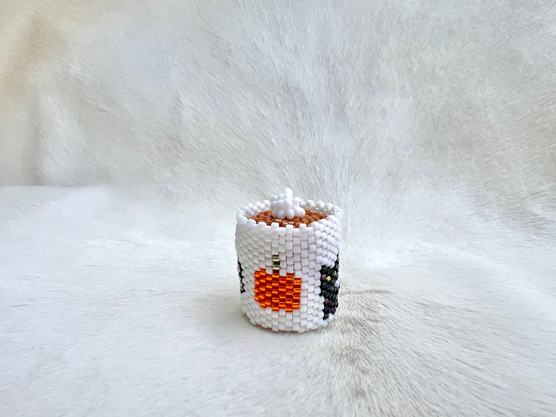 Small white beaded mug with a pumpkin design on a white fur background