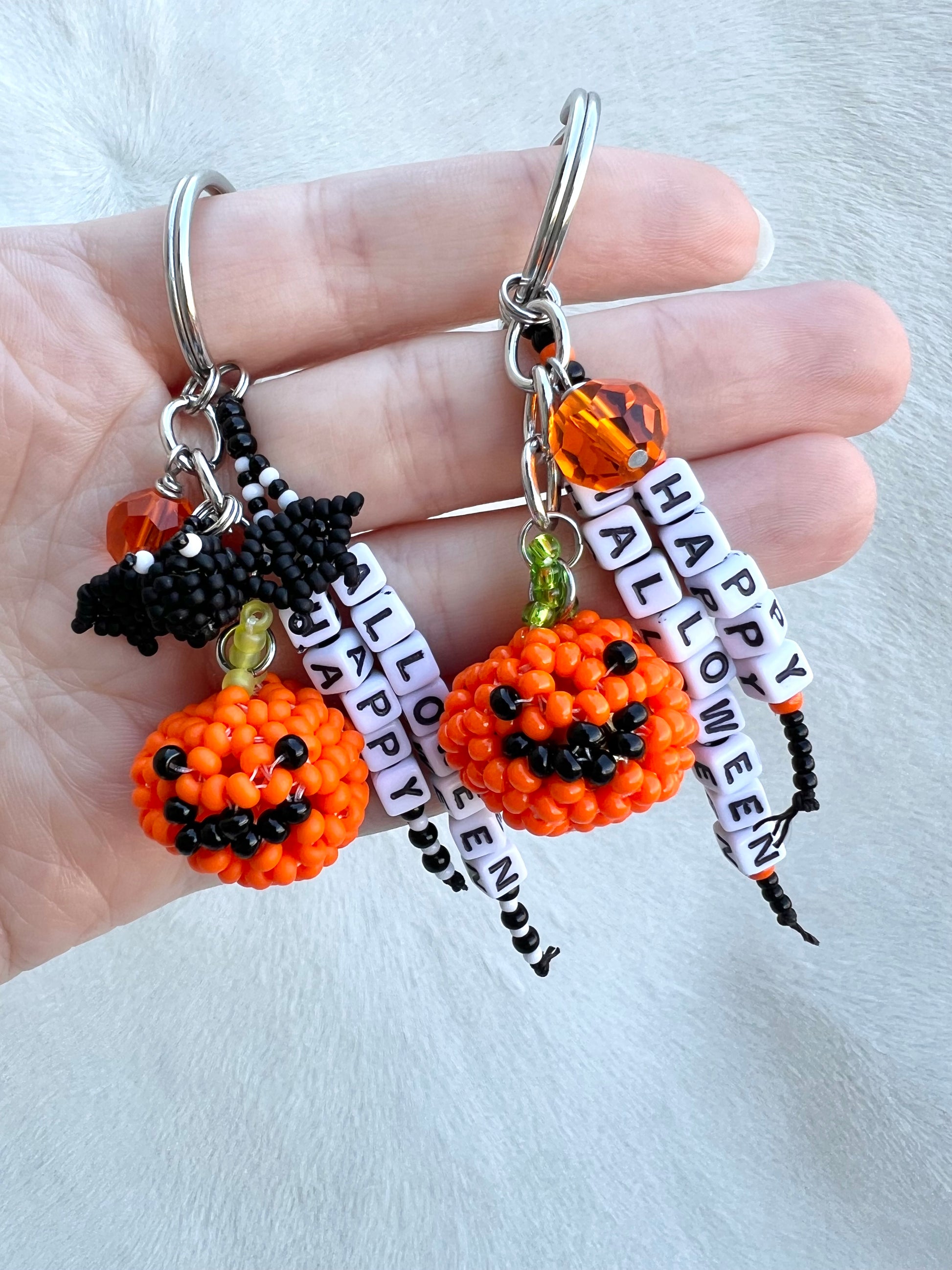 Halloween-themed keychains with pumpkins, bat and beads on a hand against a white background