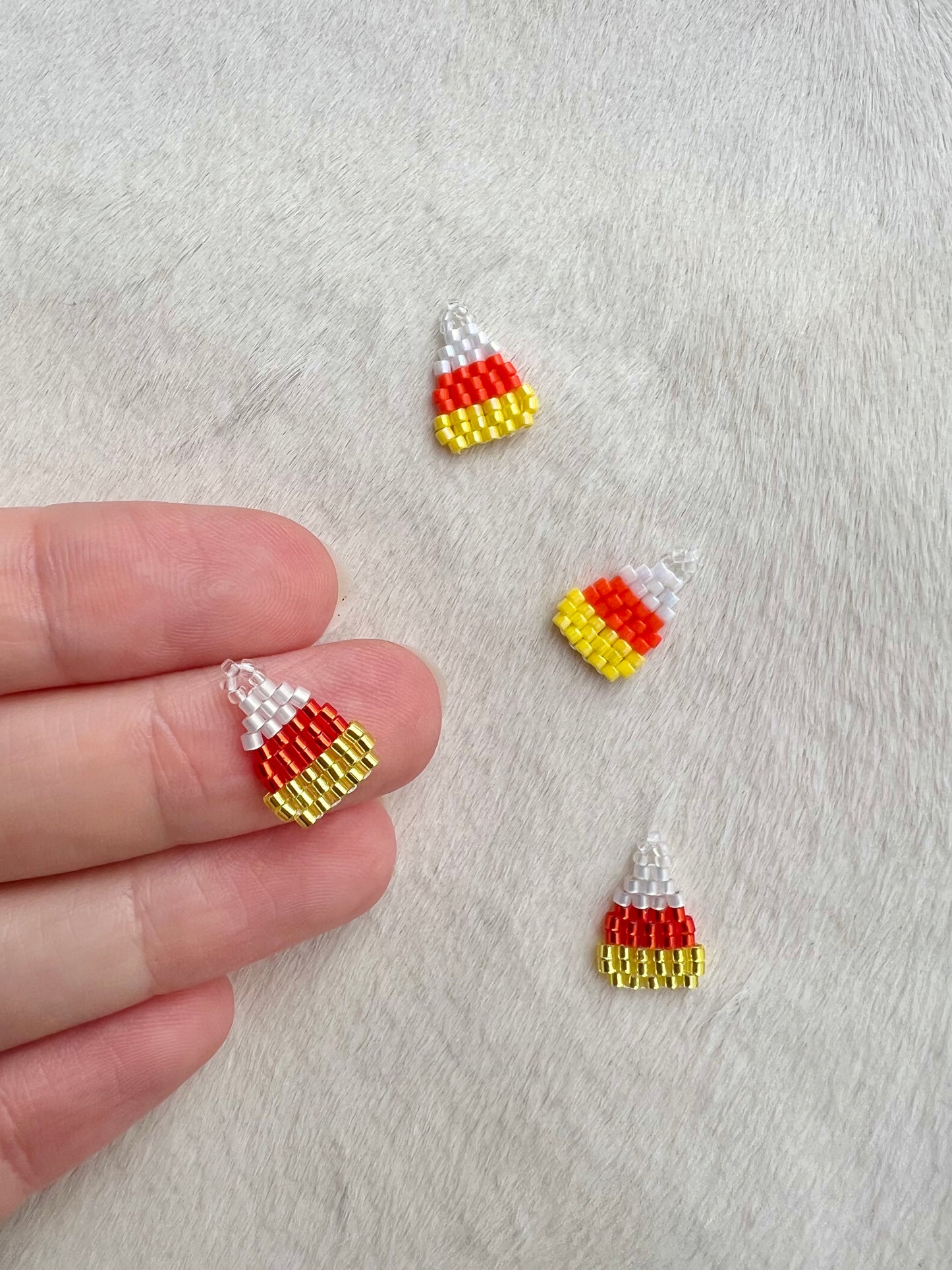 Candy corn-shaped beaded charms on a textured surface