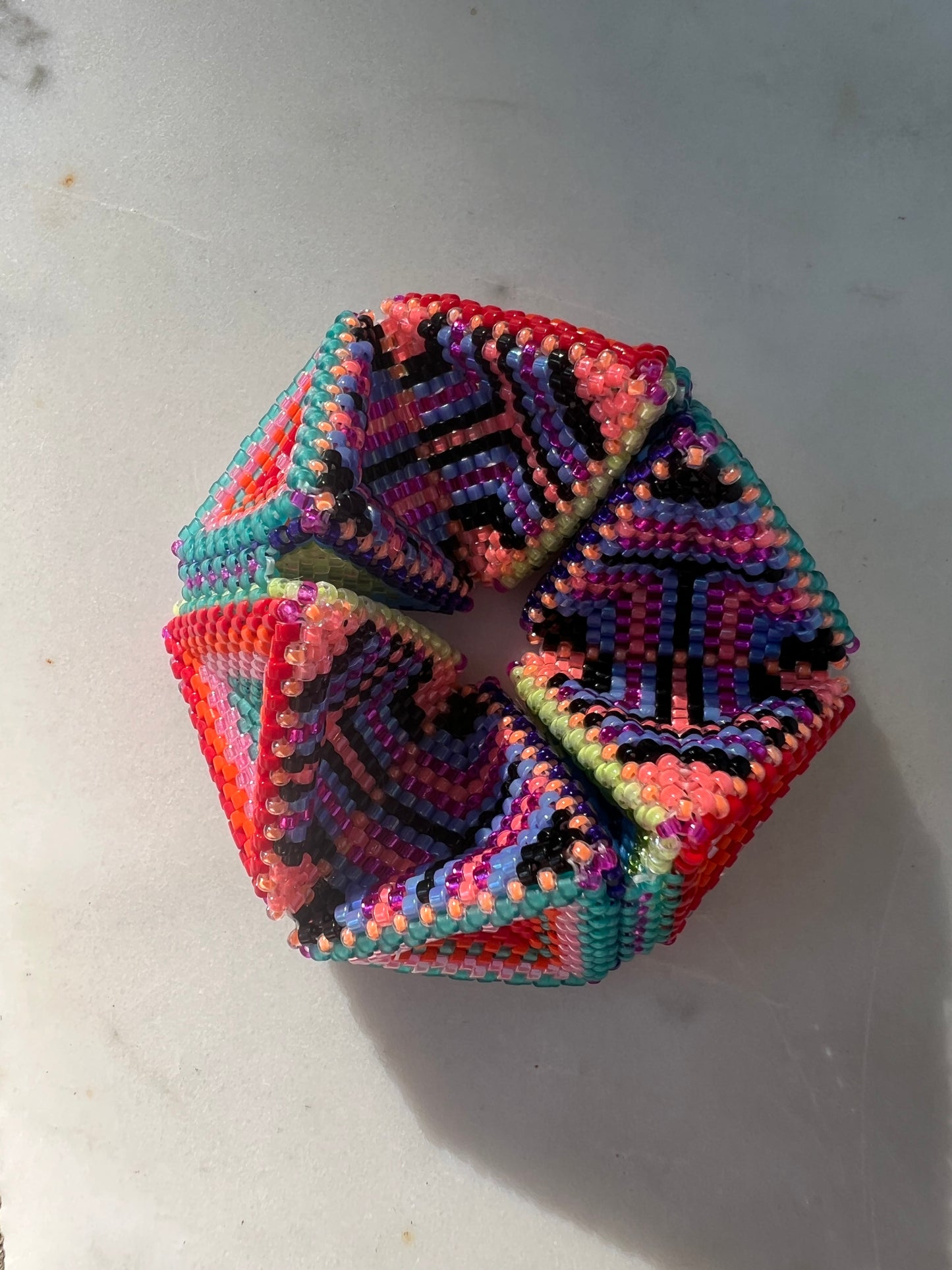 Multicolored hand beaded kaleidocycle on a light gray surface